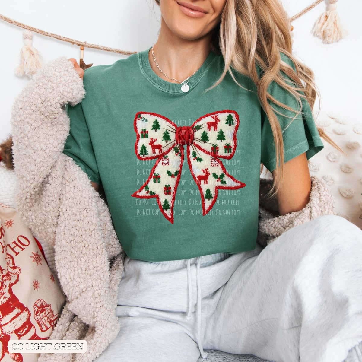 Person wearing a green t-shirt with a festive bow design, sitting on a couch.