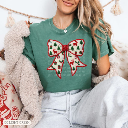 Person wearing a green t-shirt with a festive bow design, sitting on a couch.