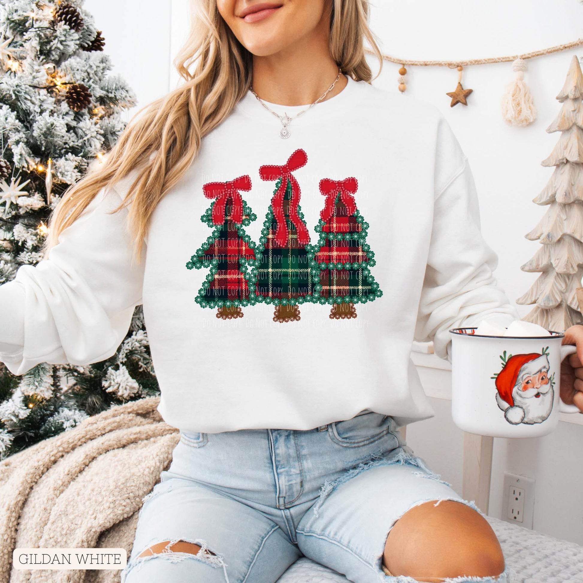 Person wearing a white sweatshirt with Christmas tree design, holding a mug with Santa Claus on it, in front of a decorated Christmas tree.