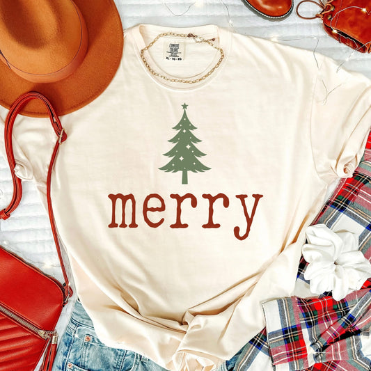 Beige t-shirt with green Christmas tree and red 'merry' text, surrounded by festive items like a hat, purse, and plaid fabric.