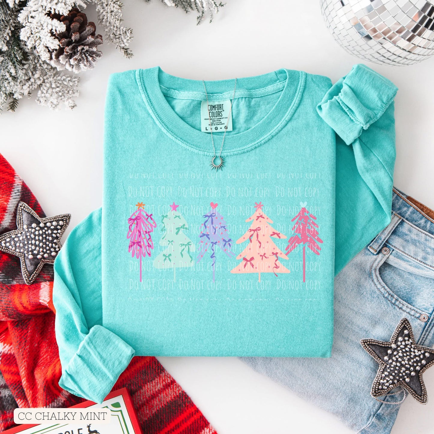 Turquoise sweatshirt with Christmas tree design on a white surface with festive decorations.