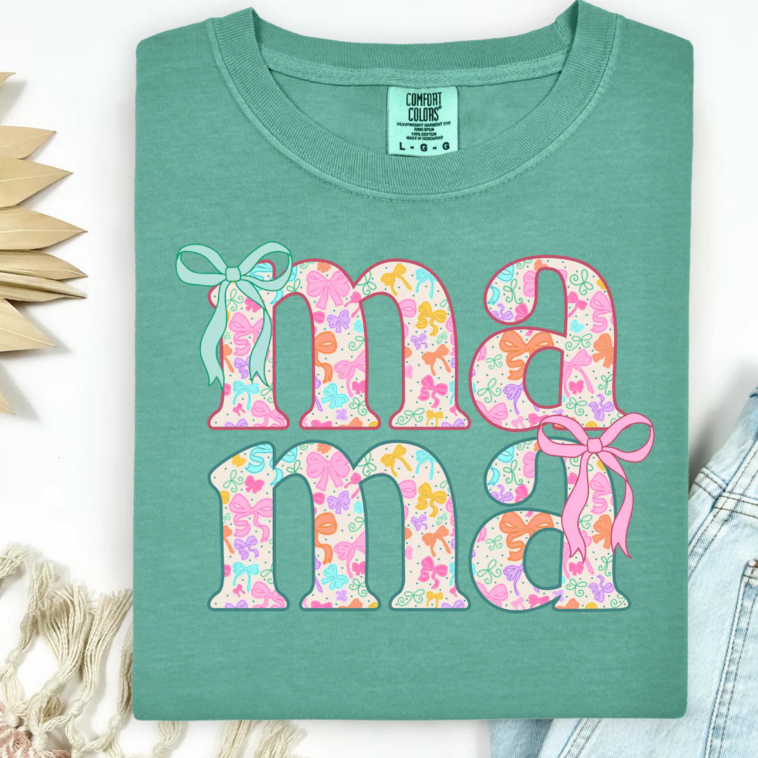 Green t-shirt with floral 'ma ma' text and ribbons on a white background