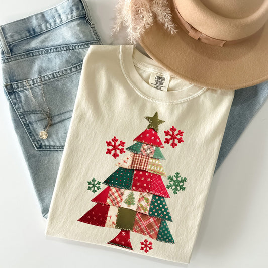 White t-shirt with a Christmas colored patchwork Christmas tree design, denim jeans, and a beige hat on a white background.