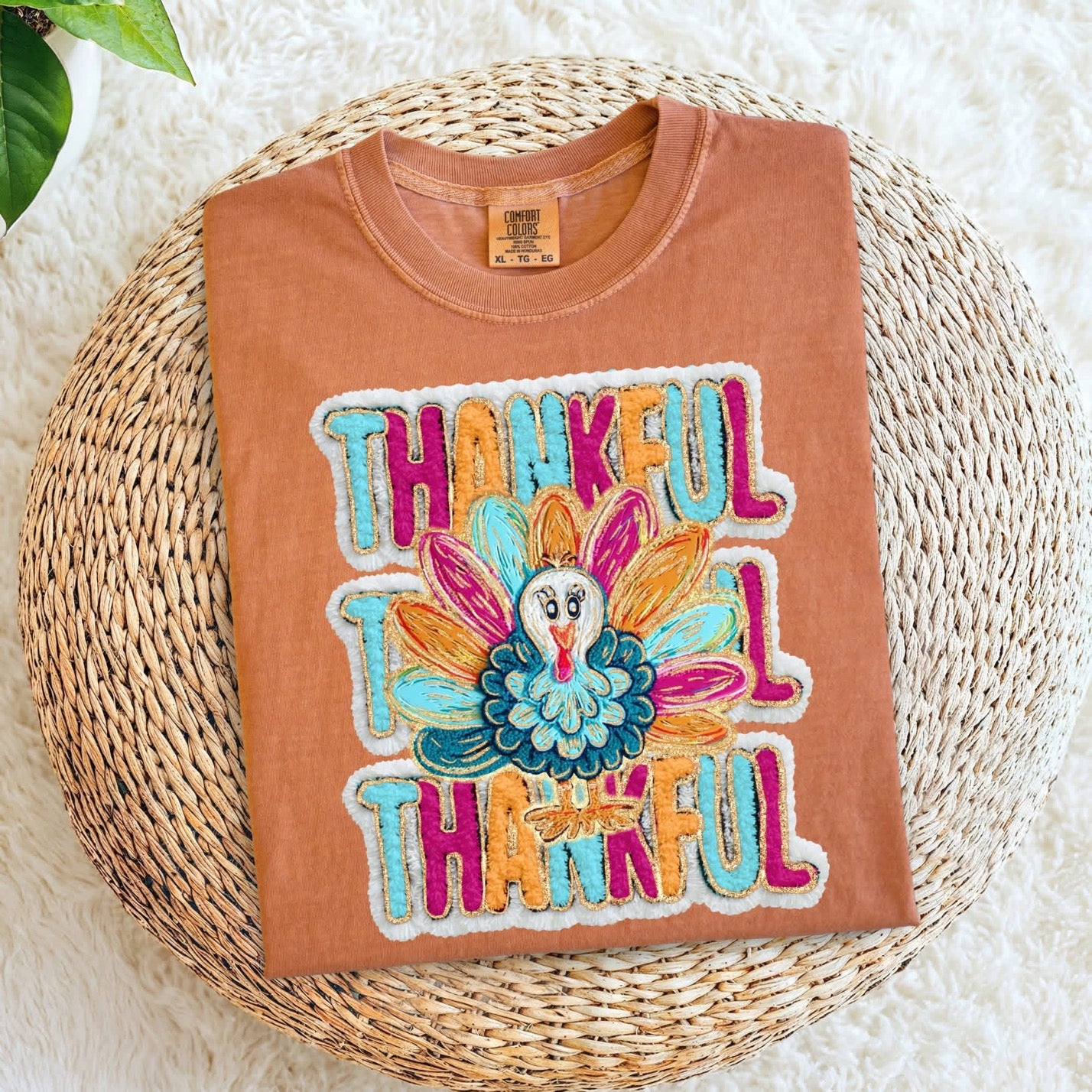 Terracotta sweatshirt with colorful 'Thankful' graphic on a woven mat