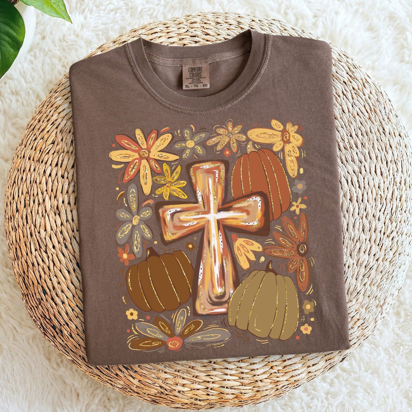Brown t-shirt with a cross and pumpkin design on a woven mat