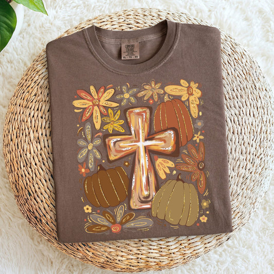 Brown t-shirt with a cross and pumpkin design on a woven mat