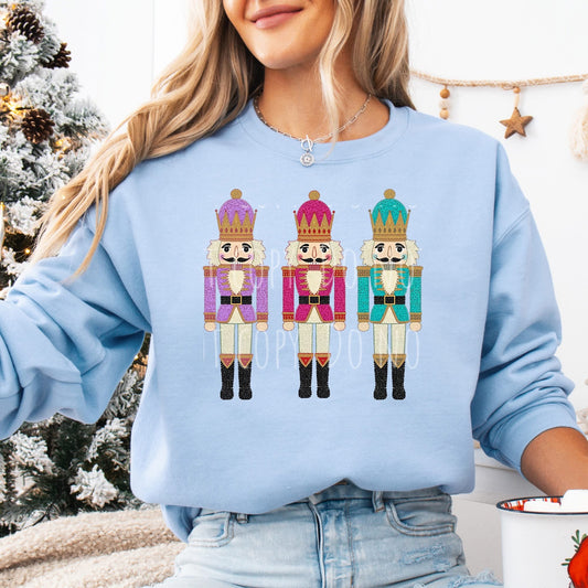 Person wearing a light blue sweatshirt with nutcracker designs in front of a Christmas tree.