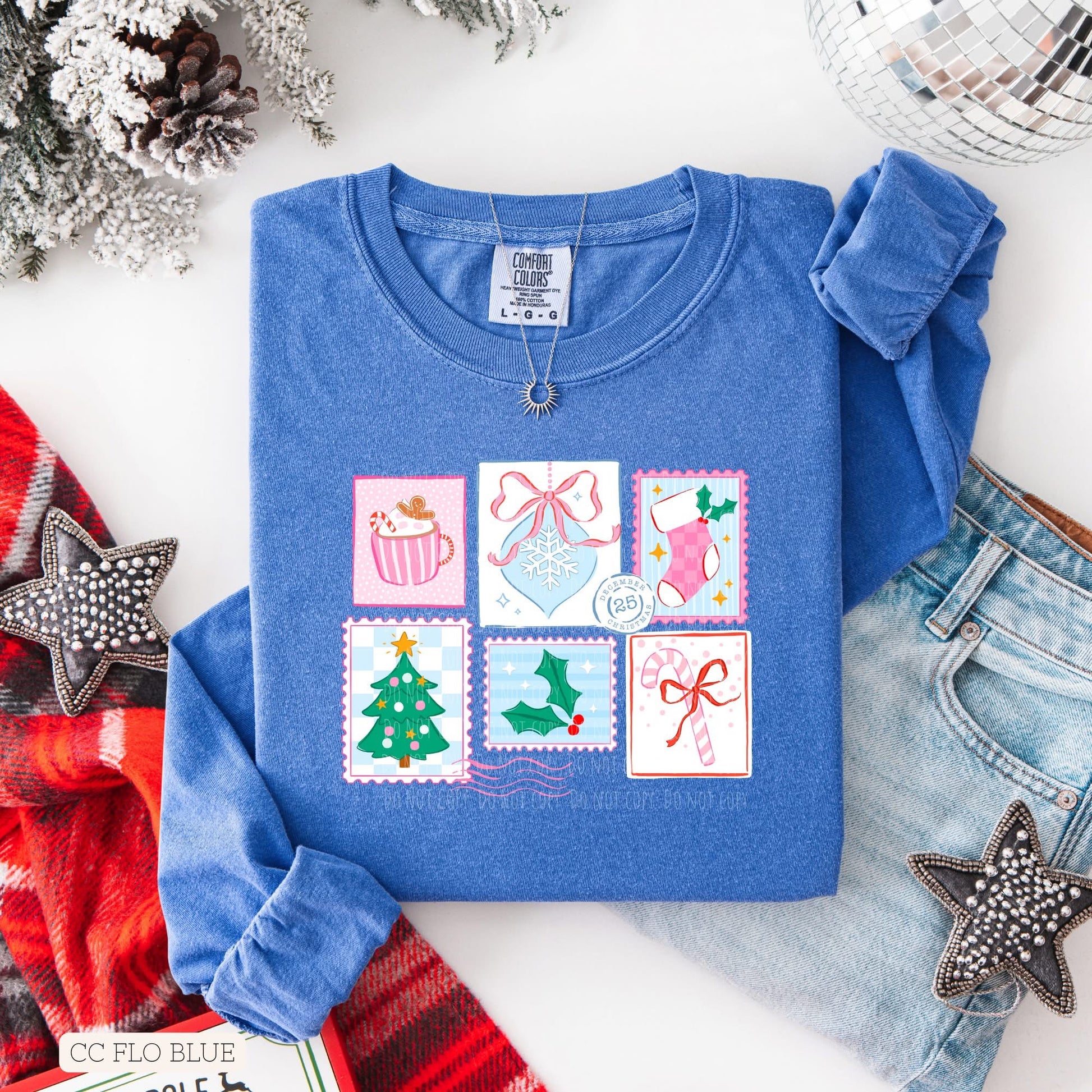 Female model with blonde hair wearing blue t-shirt with hand drawn Christmas stamps, with white background with Christmas decorations.