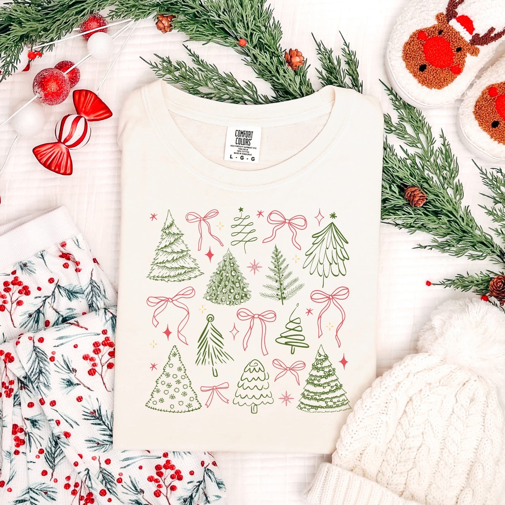 White t-shirt with Christmas tree and bow design surrounded by festive decorations on a white background