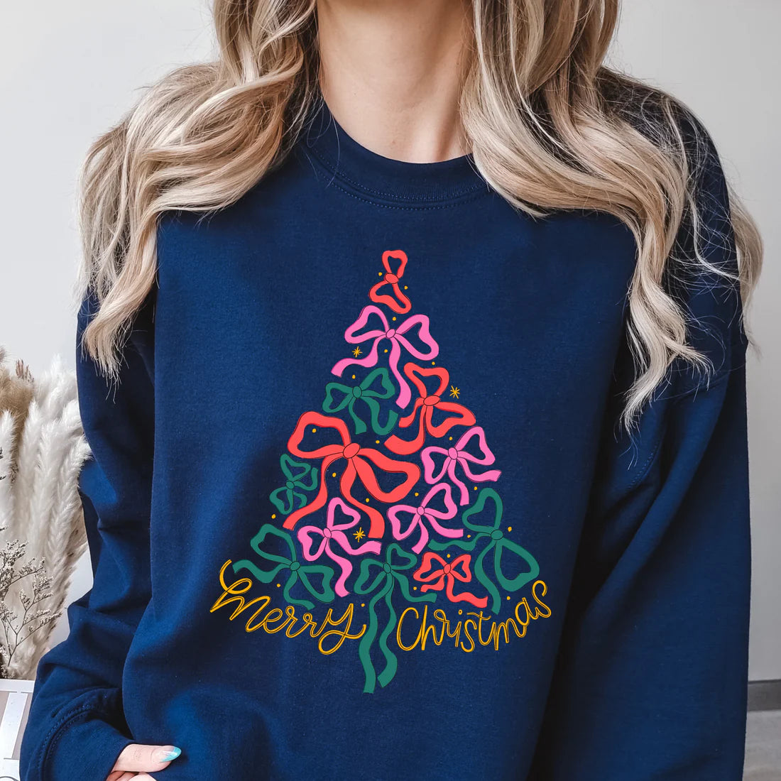 Person wearing a navy blue sweatshirt with a colorful Christmas tree design and 'Merry Christmas' text.