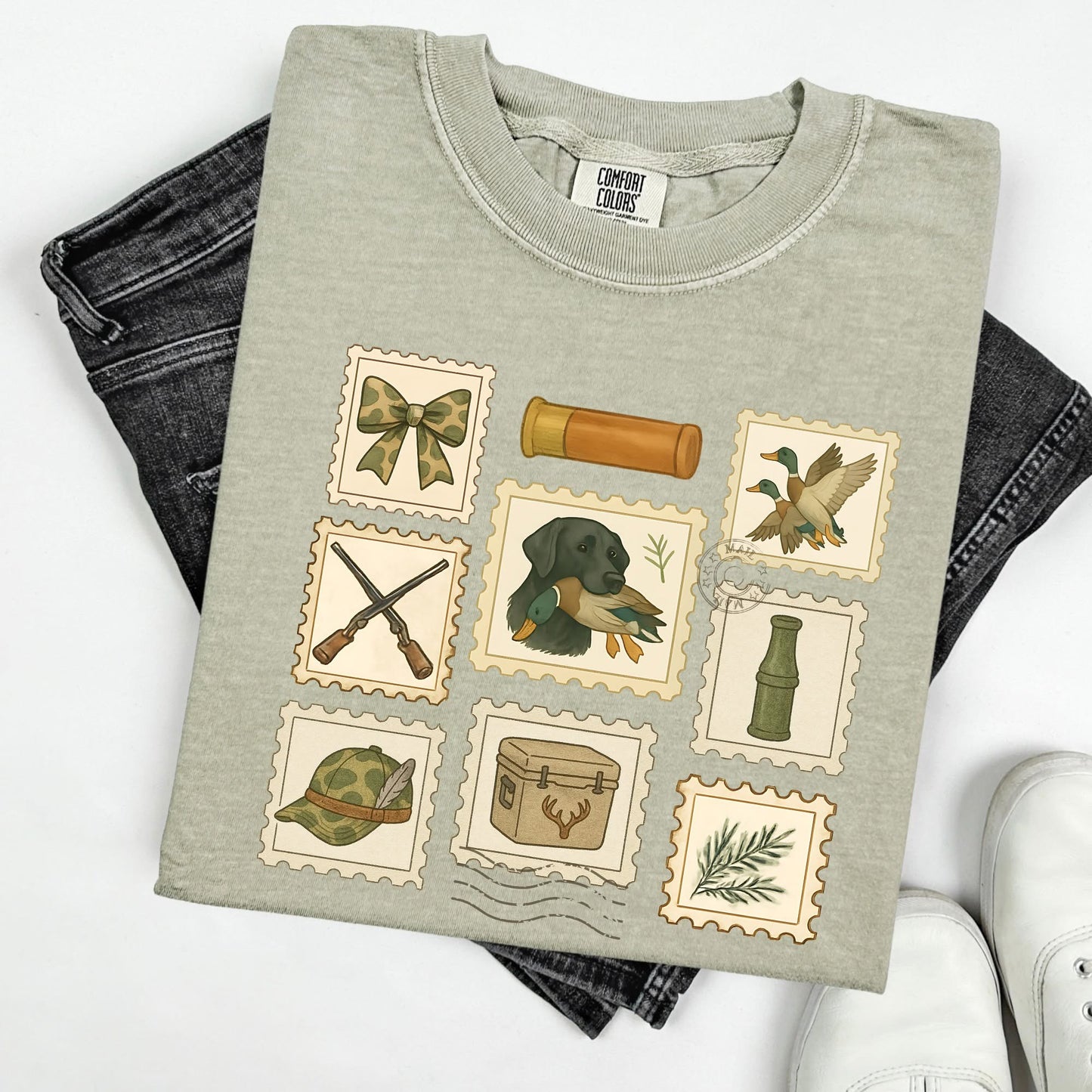 Folded gray/green  t-shirt with hunting-themed stamps with folded jeans on a white background