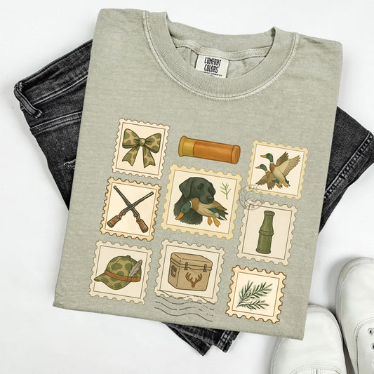 Folded gray/green  t-shirt with hunting-themed stamps with folded jeans on a white background