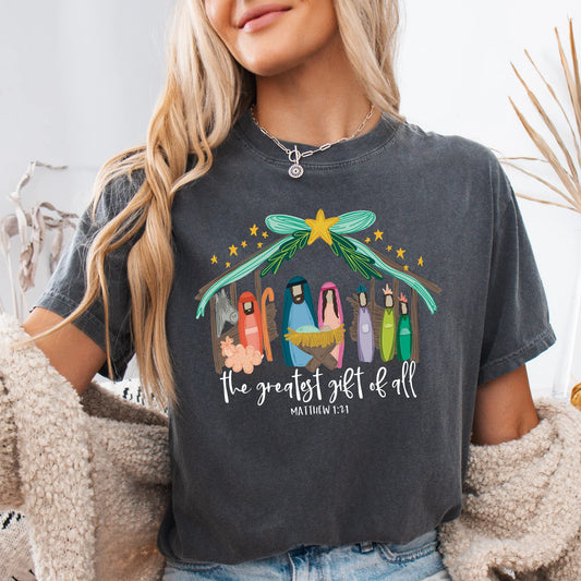 Person wearing a dark gray t-shirt with a colorful nativity scene design and text.